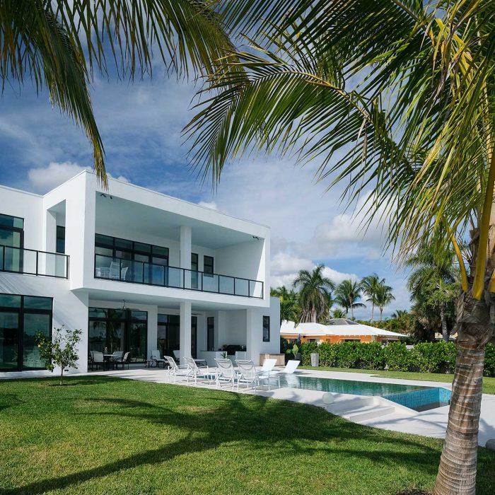 Modern beachfront house with pool and palm trees.