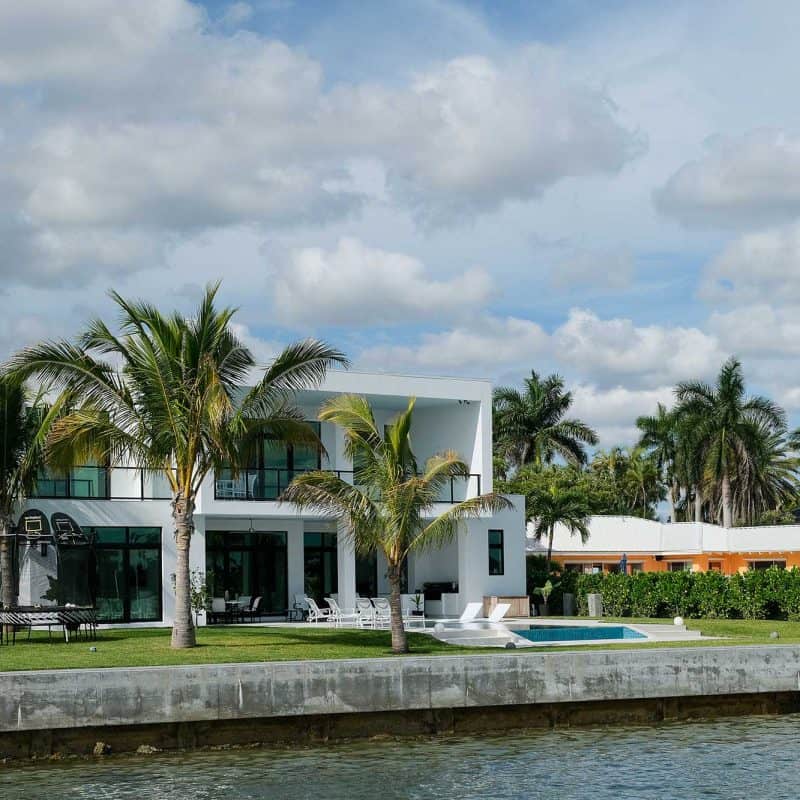 Modern waterfront house with palm trees and pool.