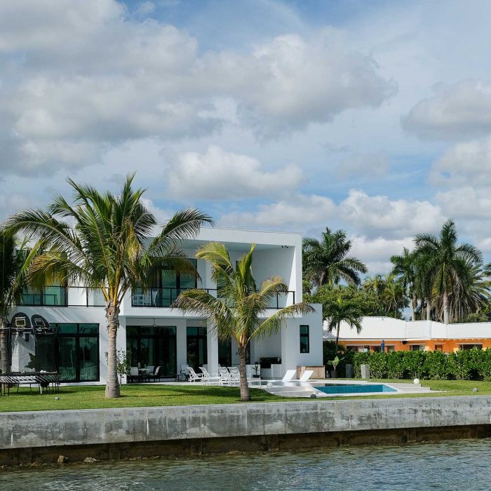 Modern waterfront house with palm trees and pool.