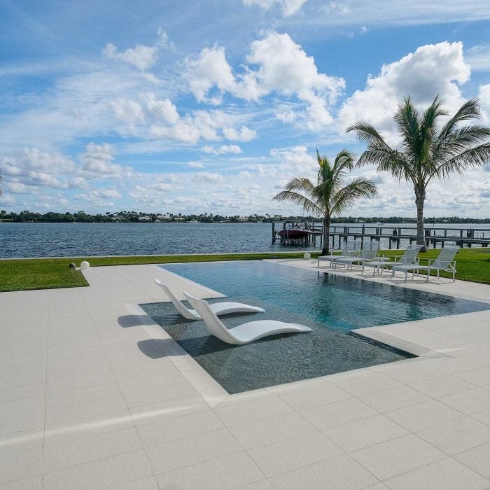 Luxury pool overlooking serene waterfront and palm trees.