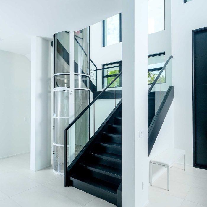 Modern staircase and glass elevator in bright hallway.