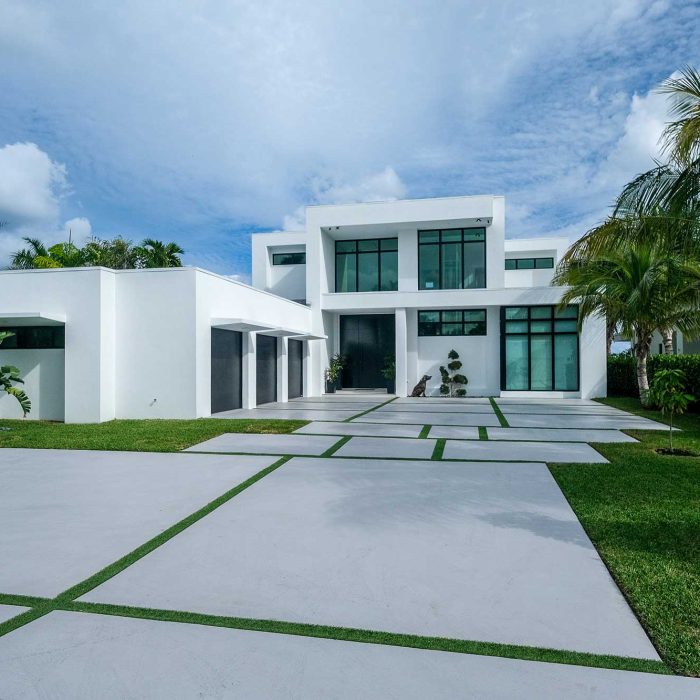 Modern white house with palm trees and driveway.