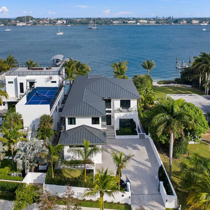 Luxury waterfront mansion with tennis court and palm trees.