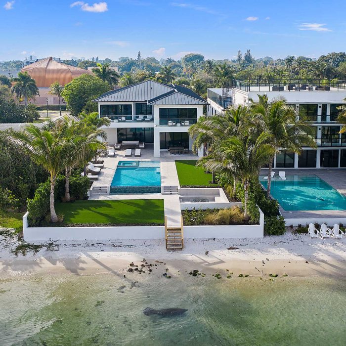 Luxury beachfront mansion with pool and palm trees.