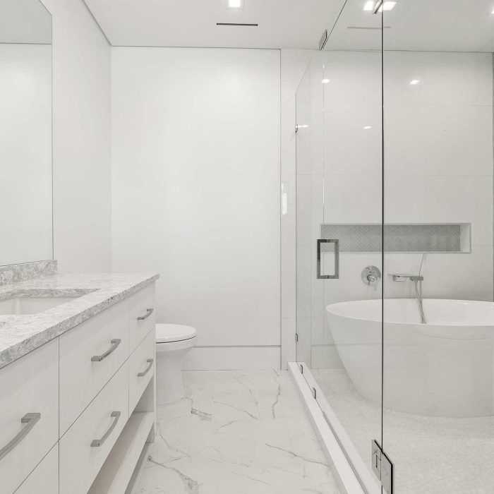 Modern white bathroom with freestanding tub and glass shower.