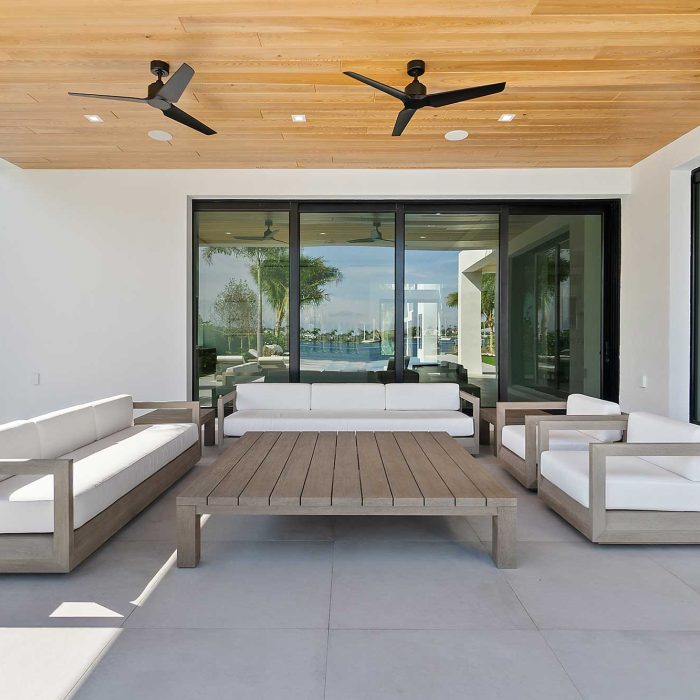 Modern outdoor patio with white furniture and ceiling fans.