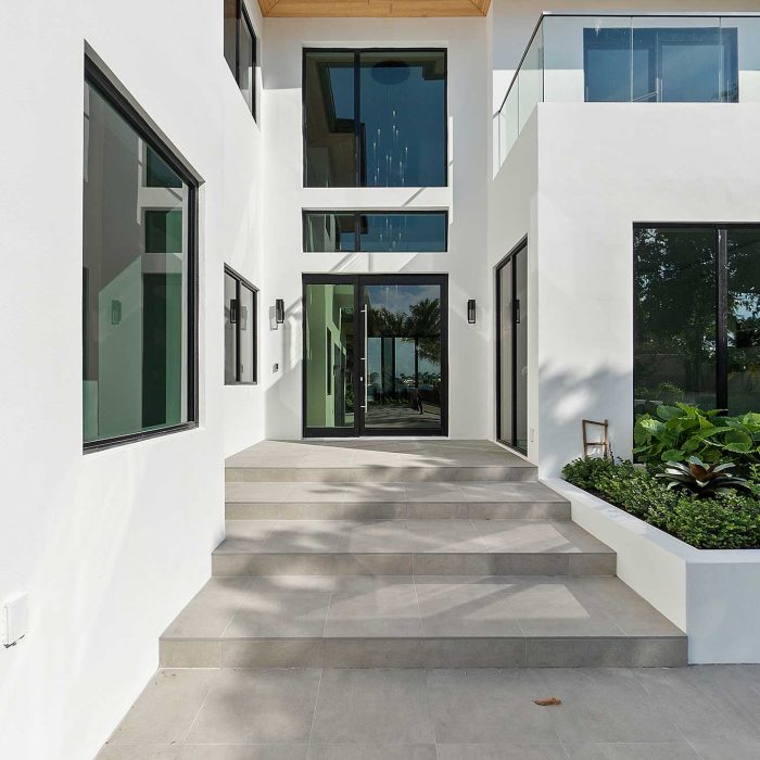 Modern house entrance with glass doors and greenery.