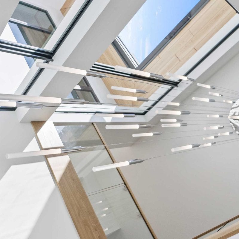 Modern chandelier beneath skylight with geometric design.