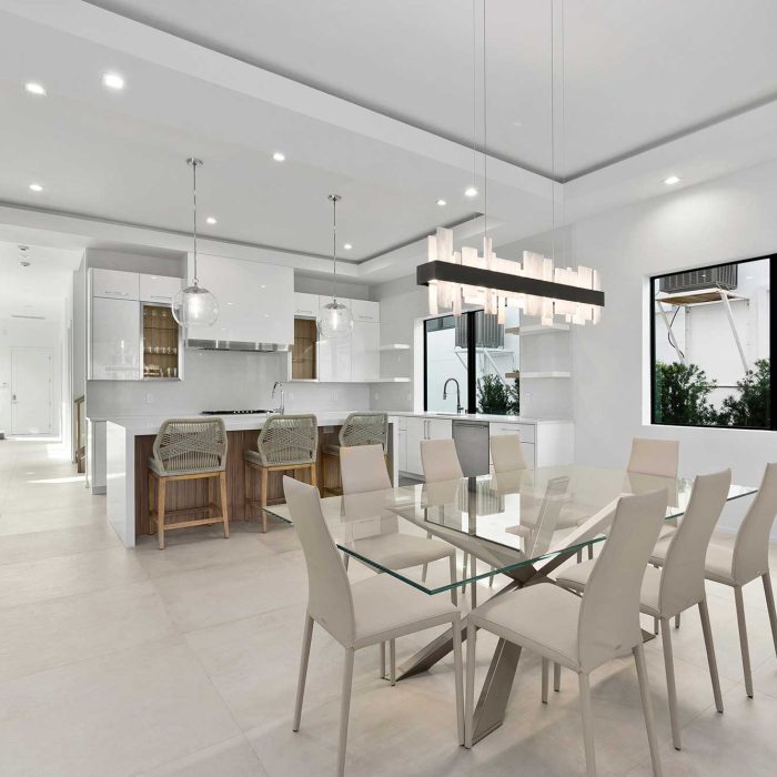 Modern kitchen with glass dining table and pendant lights.
