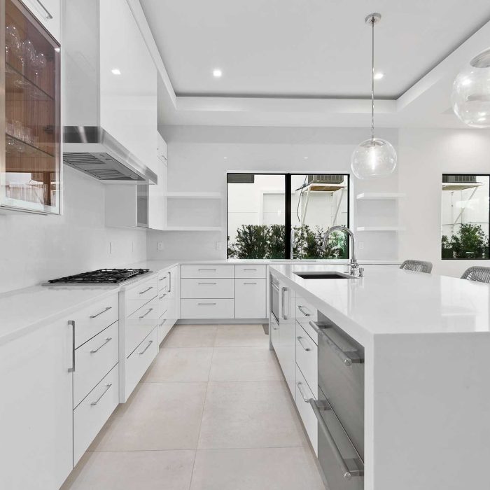 Modern white kitchen with island and pendant lights.