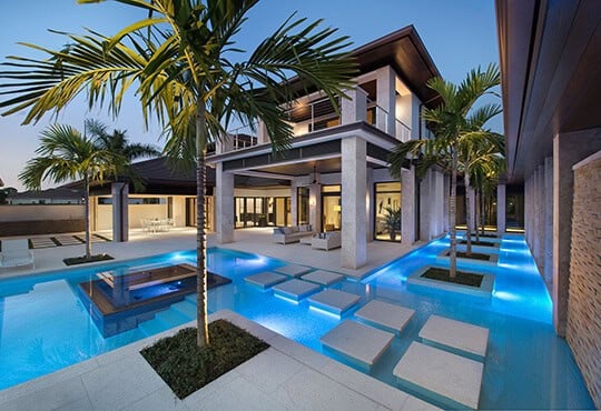 Modern house with illuminated pool and palm trees.