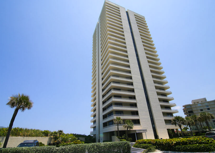 Tall condo building with palm trees and blue sky.