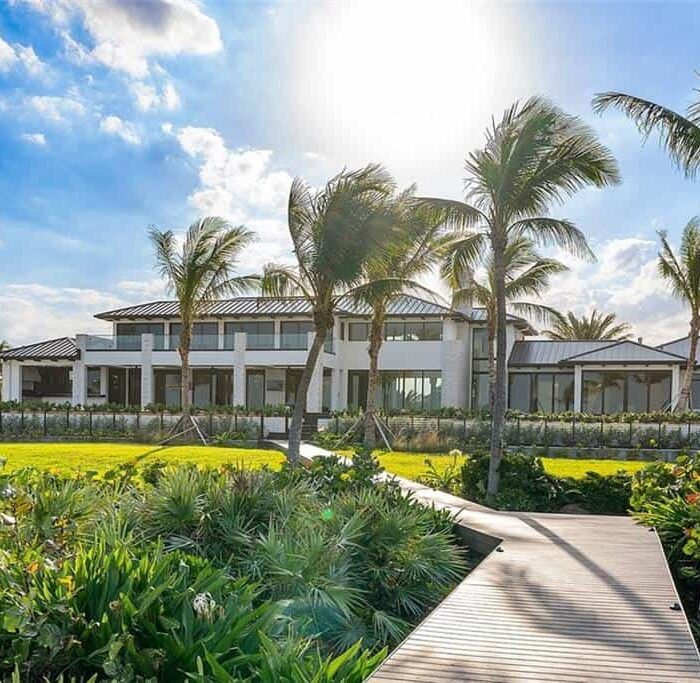 Luxury beachfront house with palm trees and garden.
