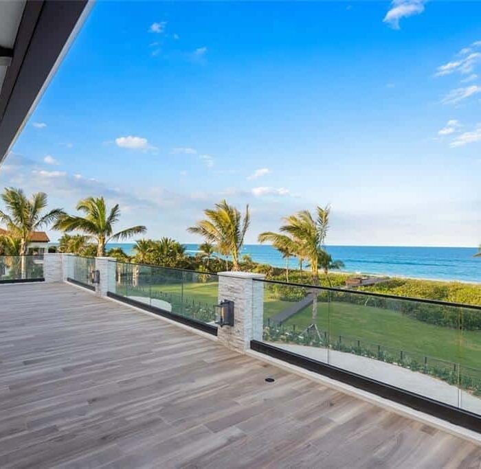 Spacious oceanfront balcony with palm trees and sea view.