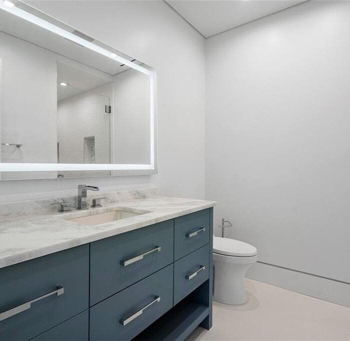 Modern bathroom with illuminated mirror and gray vanity.