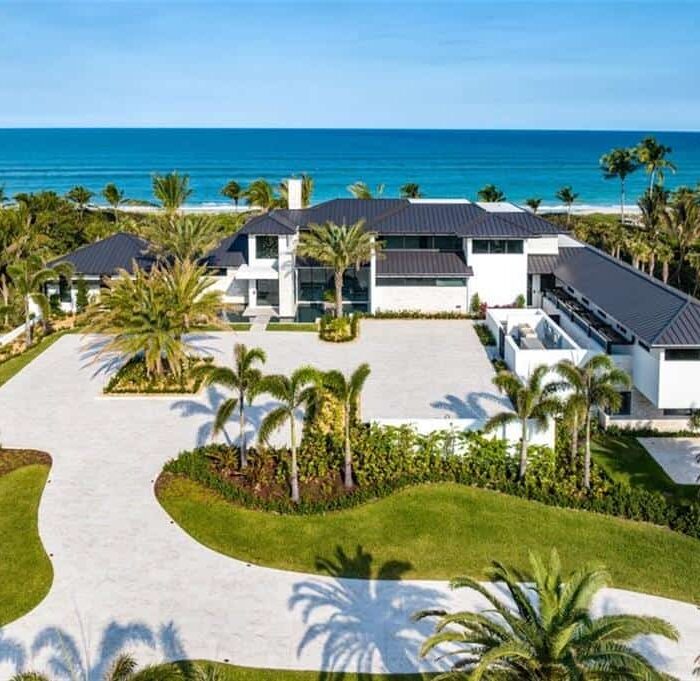 Luxurious beachfront mansion with palm trees and ocean view.