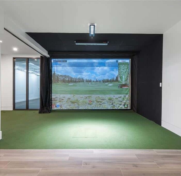 Home golf simulator with green turf and screen