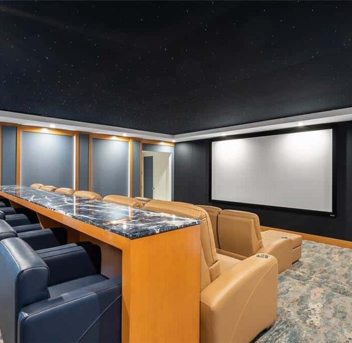 Luxury home theater with reclining chairs and projector screen.