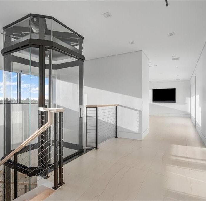 Modern home interior with glass elevator and hallway.