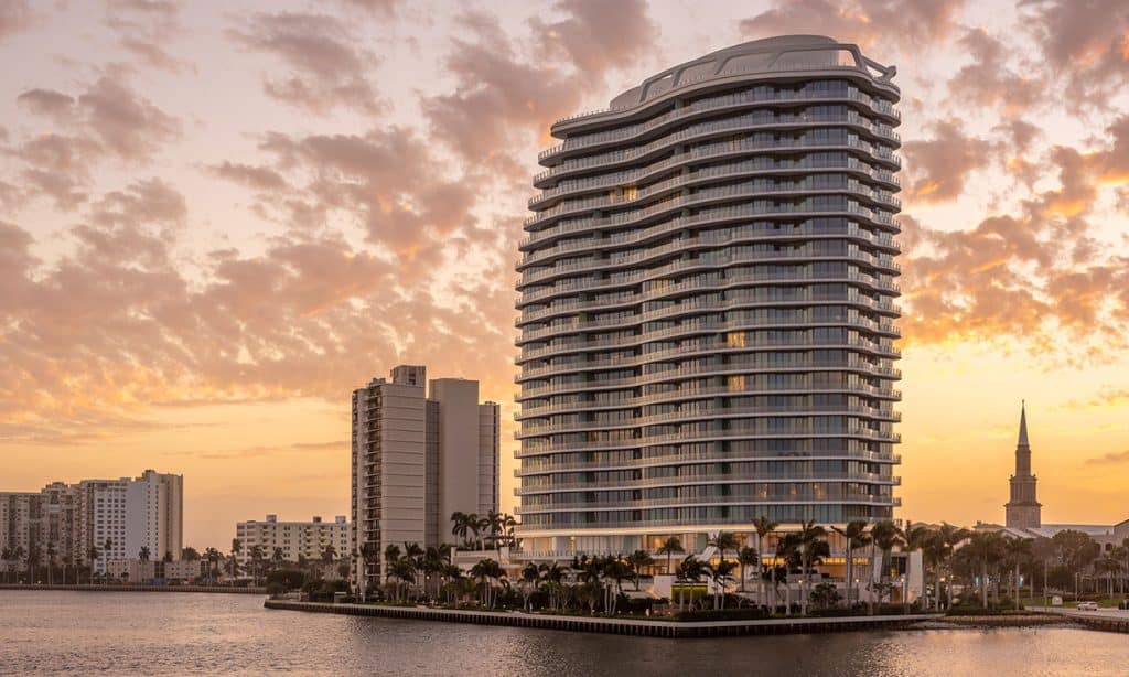 Modern waterfront skyscraper at sunset with palm trees.