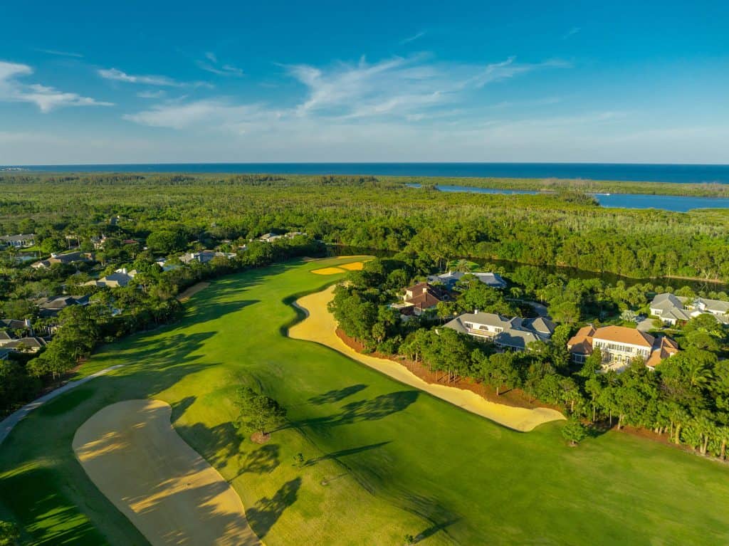 Aerial view of golf course and houses by ocean.