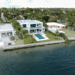 Luxury waterfront home with pool and palm trees.