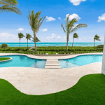 Oceanfront pool with palm trees and blue sky.