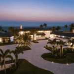 Beachfront mansion at sunset with palm trees.