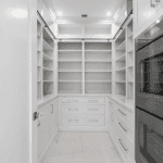 Modern kitchen pantry with white shelving and cabinets.